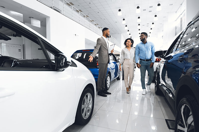 An car salesmen shows a couple around the inside of a car dealership